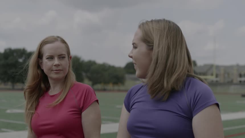 Two women walk and talk by a field