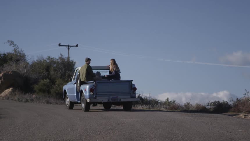 Two people ride in the back of a truck in the daytime
