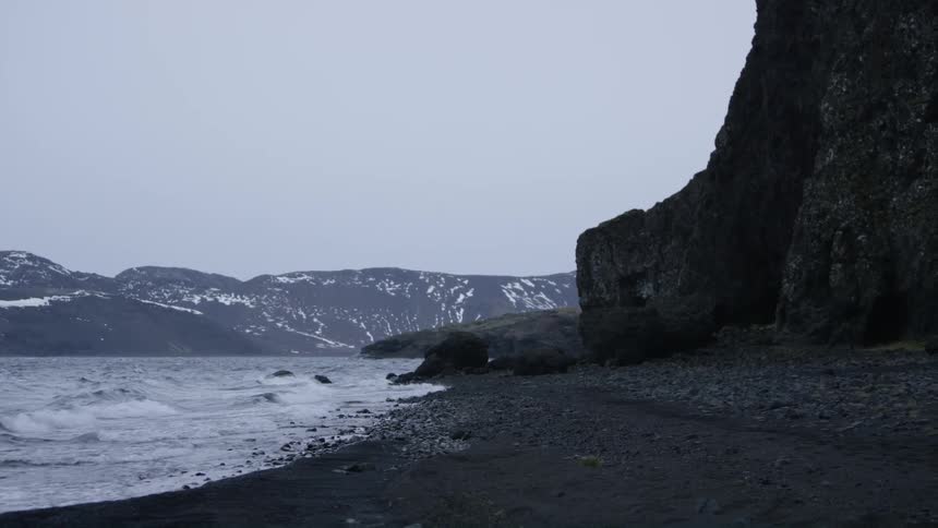 Waves crashing on the shore next to a tall rock