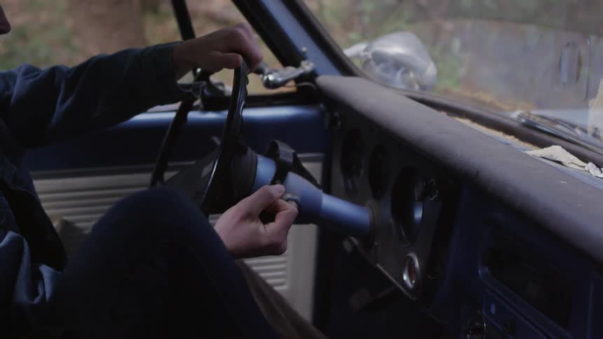 A person shifts a truck into gear as another person puts their feet on the dash