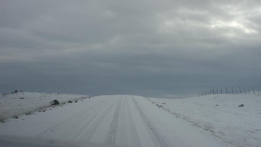 A road covered by snow is traveled down on an overcast day