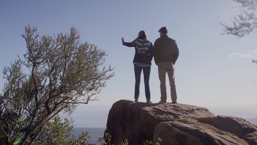 Two people stand on a rock and look at the scenery below