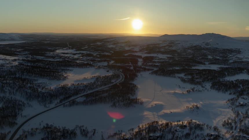 The field and forests below are covered with snow before the sun sets