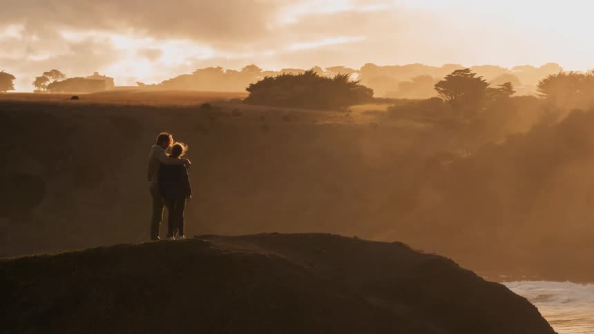 A father and daughter take in a coastal view from a hilltop