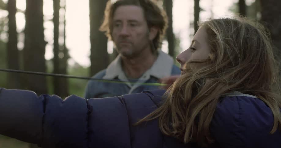 A man shows a girl how to shoot an arrow