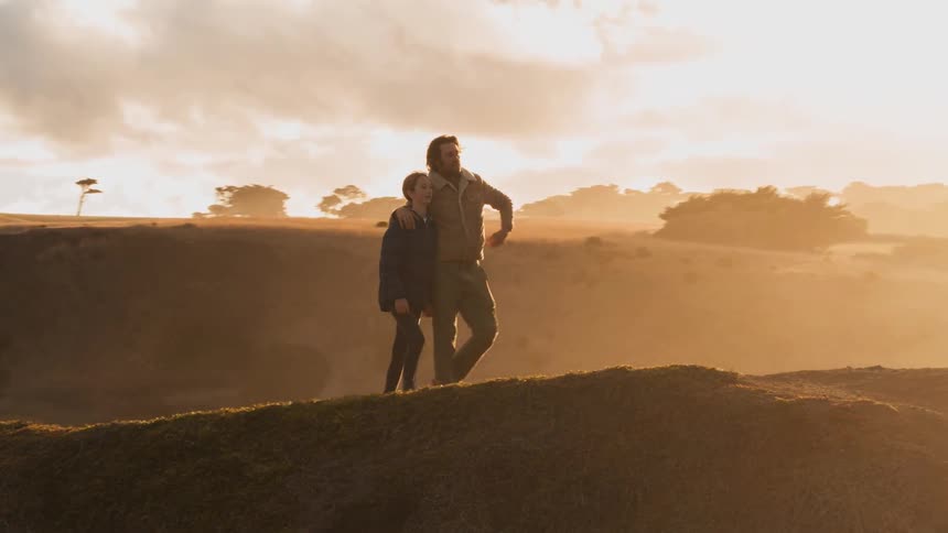 Two people hug and walk atop a hill