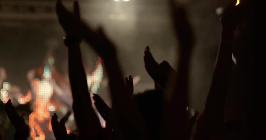 People at a concert are raising their hands above their heads and clapping