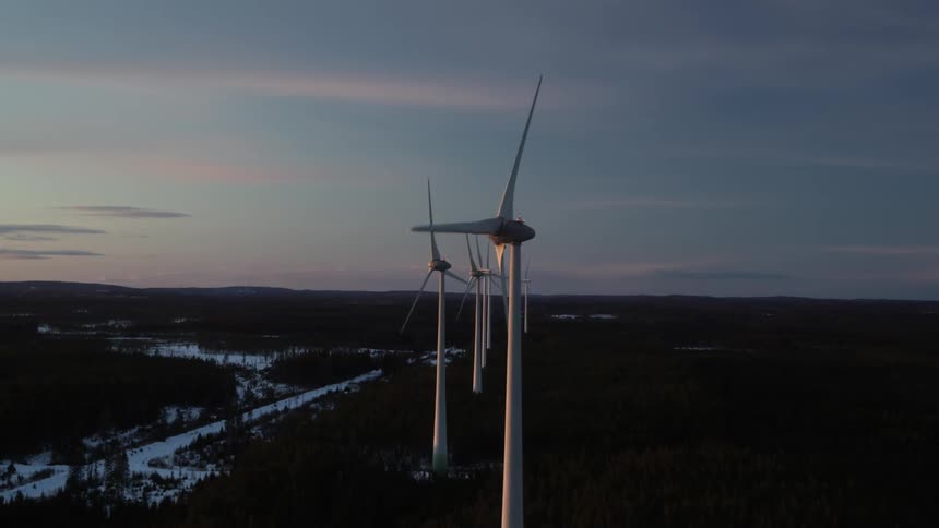 A row of wind turbines are turning at dusk