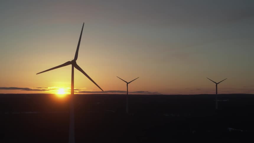 A wind turbine is spinning with the sun in the background
