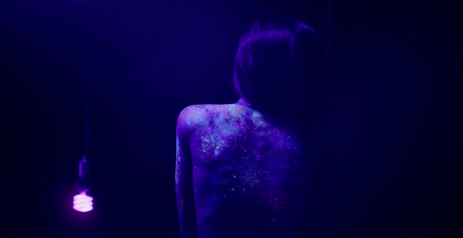 A woman with body paint is stretching in a purple lit room