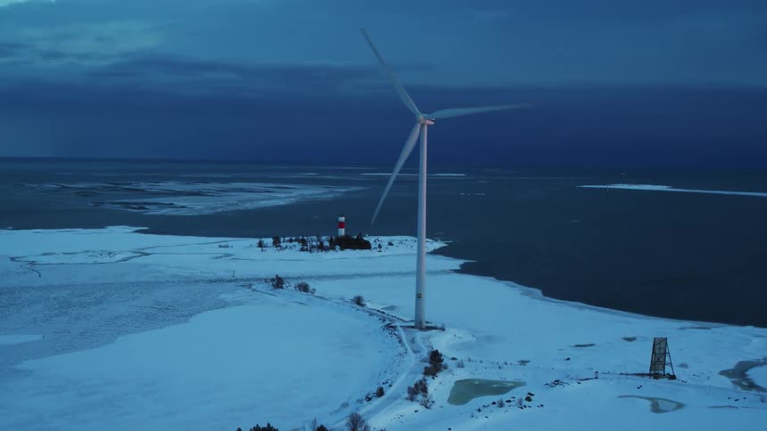 A wind turbine rotates on a snowy coast
