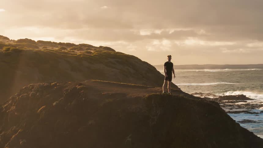 A man is standing on the edge of a cliff next to the ocean