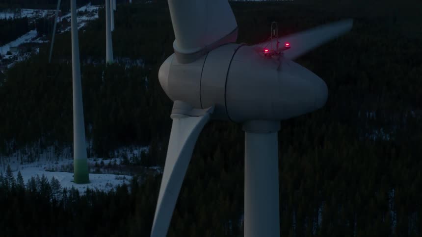 A wind turbine rotates with snow on the ground