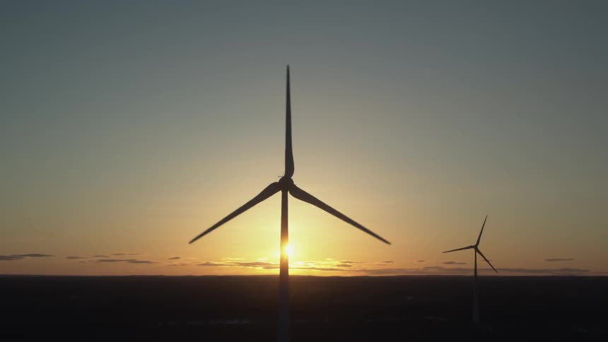 The windmills move slowly as the sun sets in the very distance