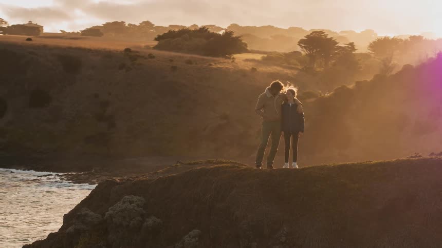 A couple take in a coastal view from a hilltop