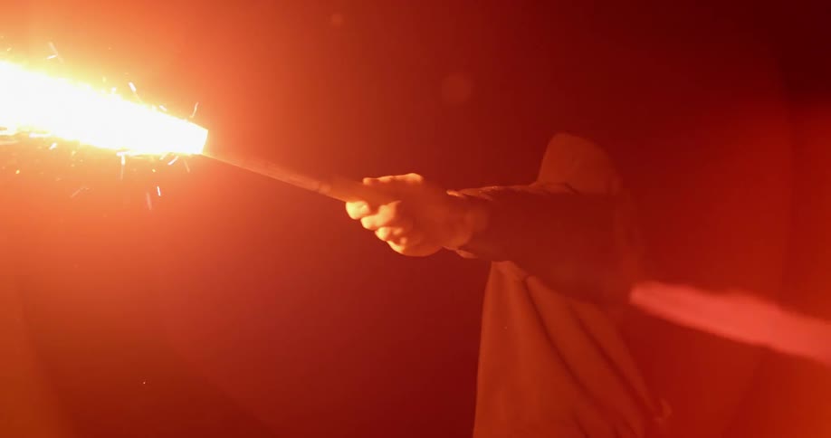 A man in a mask carries a lit flare at night
