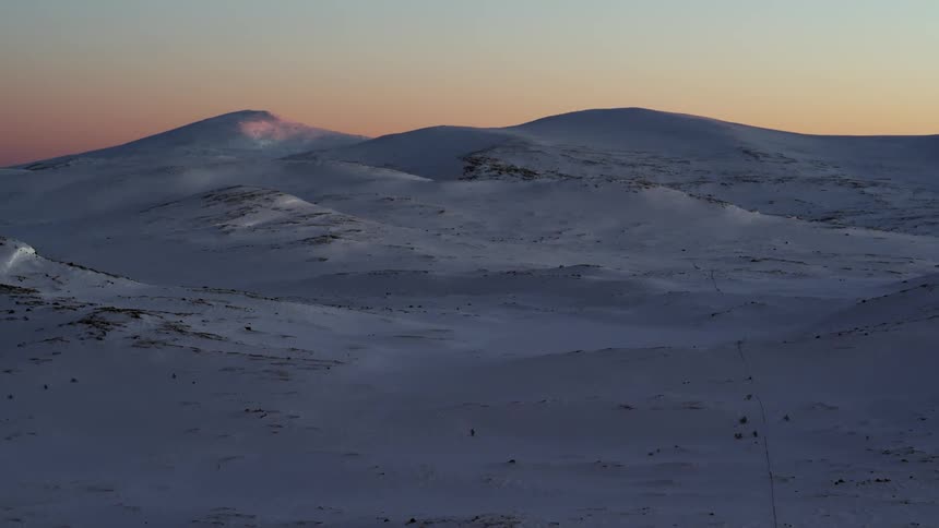 Snow covered landscape is filmed at dusk from a drone