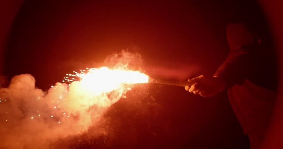 A man swings a lit flare outdoors
