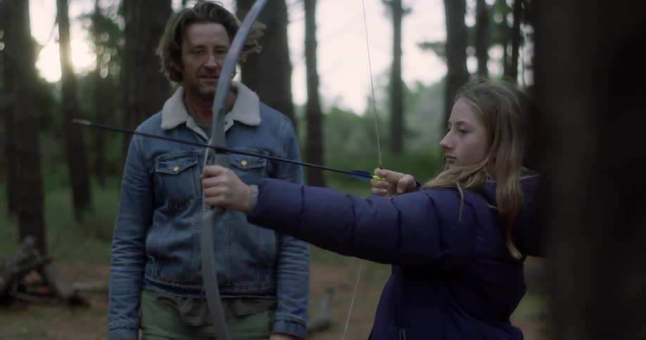 A man is showing a young girl how to shoot a bow and arrow