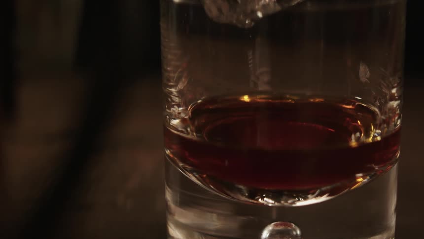 An ice cube is dropped into a glass of liquor