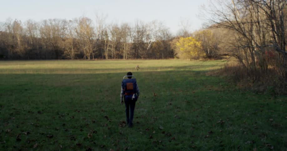 A man and a little girl in backpacks are walking through the woods