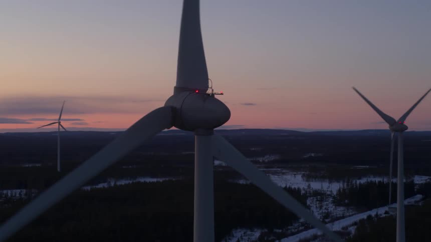 A group of wind turbines are spinning at dusk