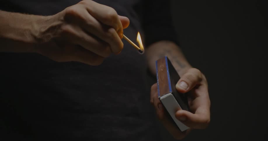 Person striking and lighting a match on match box in the dark