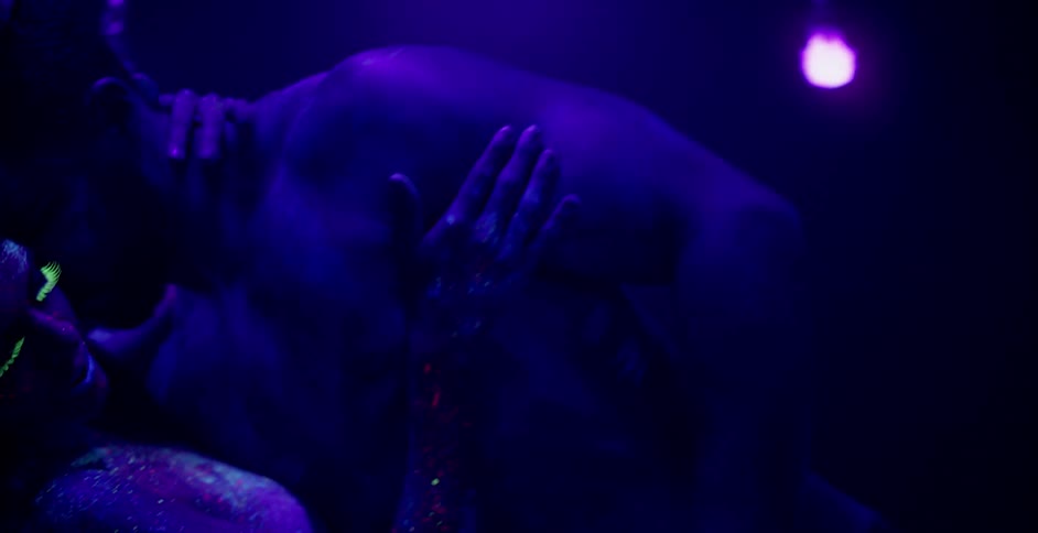 A man and woman dance together in a dark black lit room