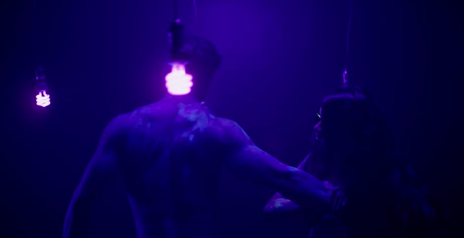 A man and woman embrace in a dark black lit room