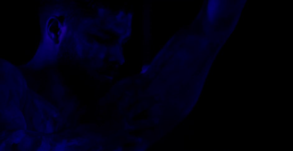 A man is rubbing his chest in a purple lit room