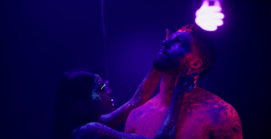 A woman touches a man covered in glowing body paint