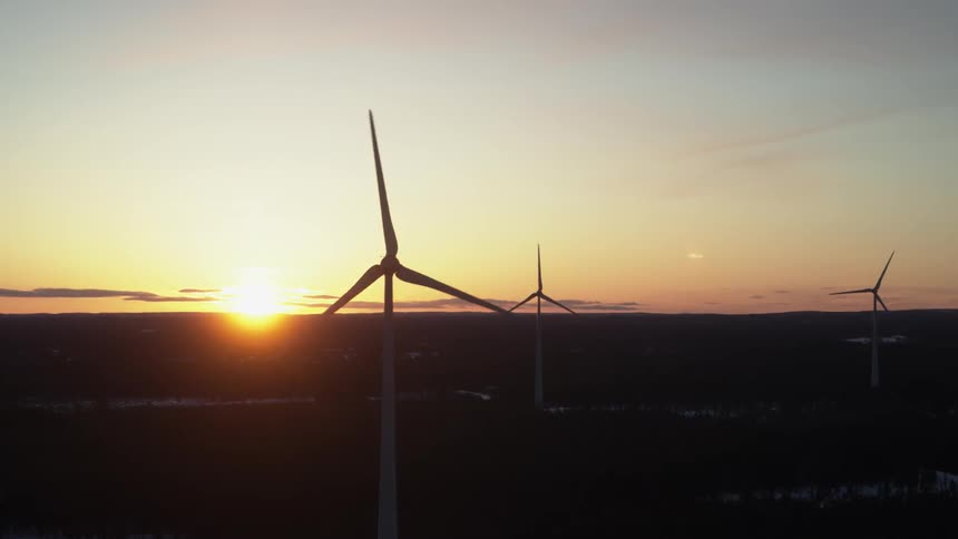Wind turbines are spinning with the sun in the distance