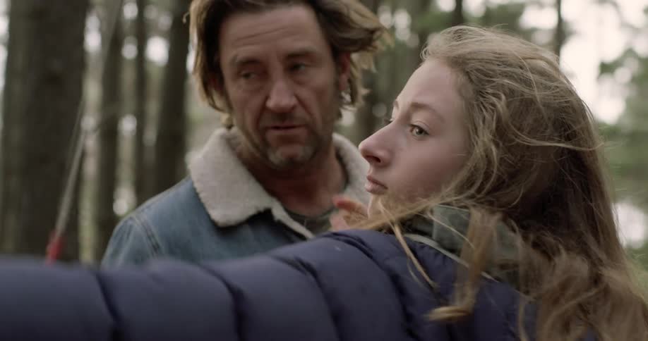 A man teaches a girl to shoot a bow and arrow in the woods