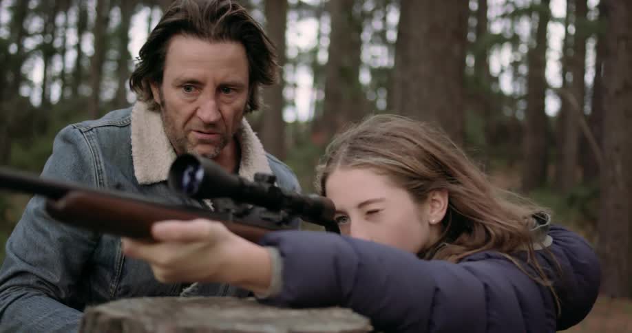 A man is teaching a young girl how to shoot a rifle