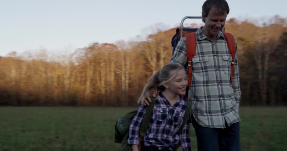 A man walks with his daughter down a field
