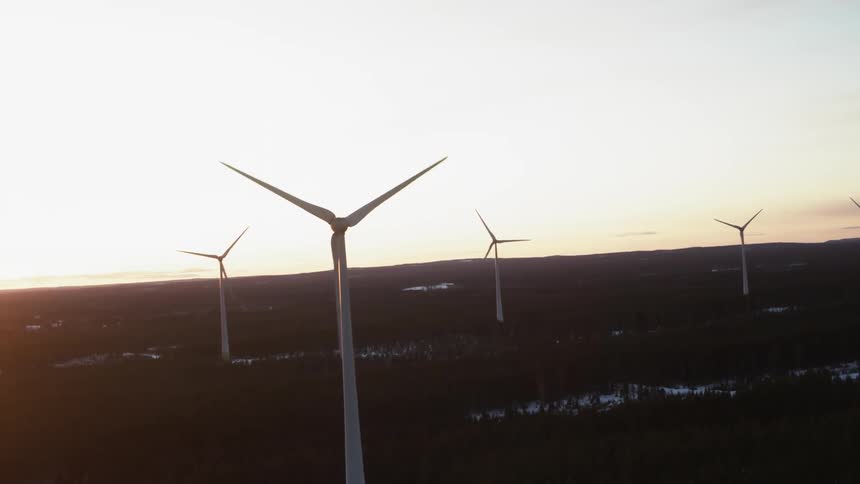 A group of wind turbines are spinning as the sun sets