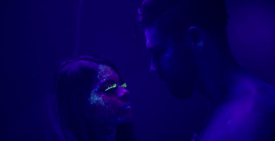 A man and woman are in a black light room dancing and hugging