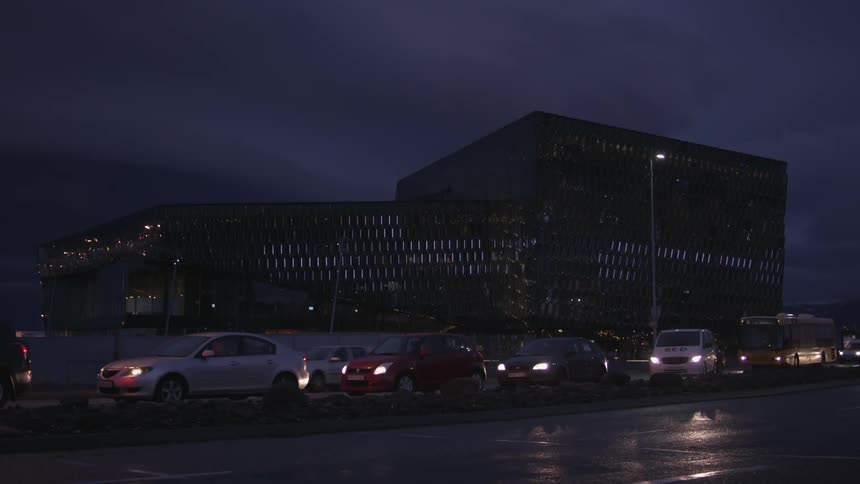 Traffic sits in a turn lane on a road near an office building at night
