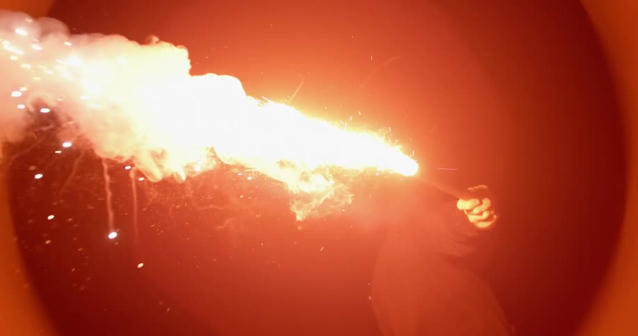 Person holding a flaming flare outside at night