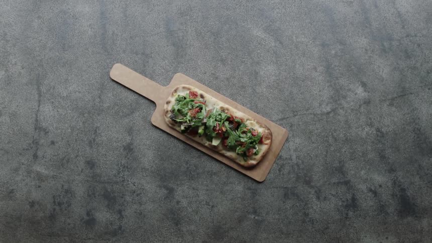 A flatbread pizza is on a wood serving plate