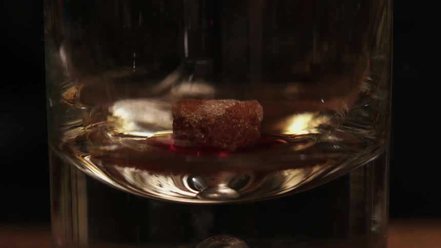 Liquor is poured into a glass with a block of brown sugar in it