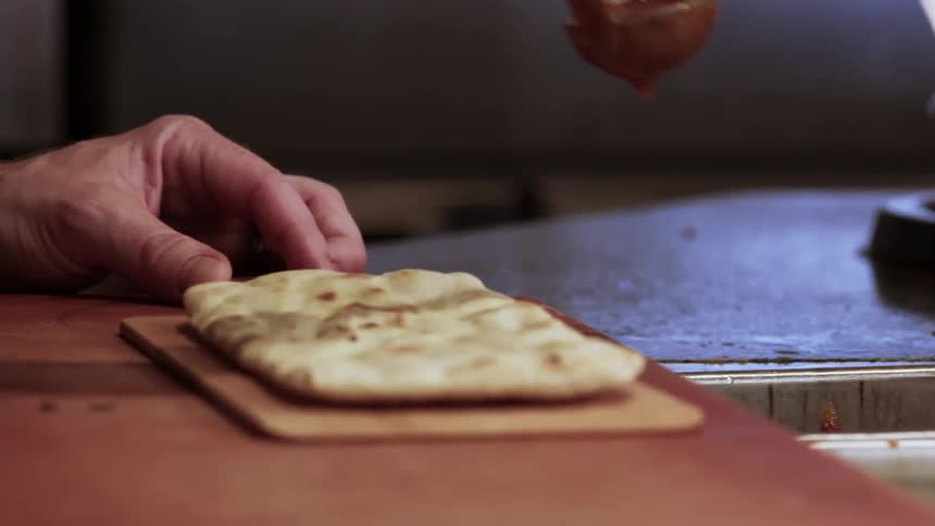 A man pours sauce onto a flatbread