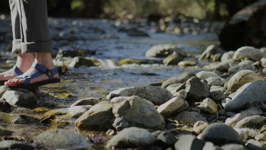 Sandal footed legs cross over shallow creek on protruding rocks