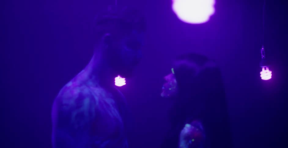A man and woman approach in a black lit room