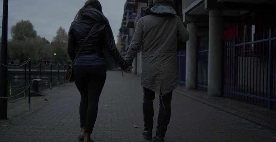 A dad carries his daughter on his shoulders and holds his wife's hand