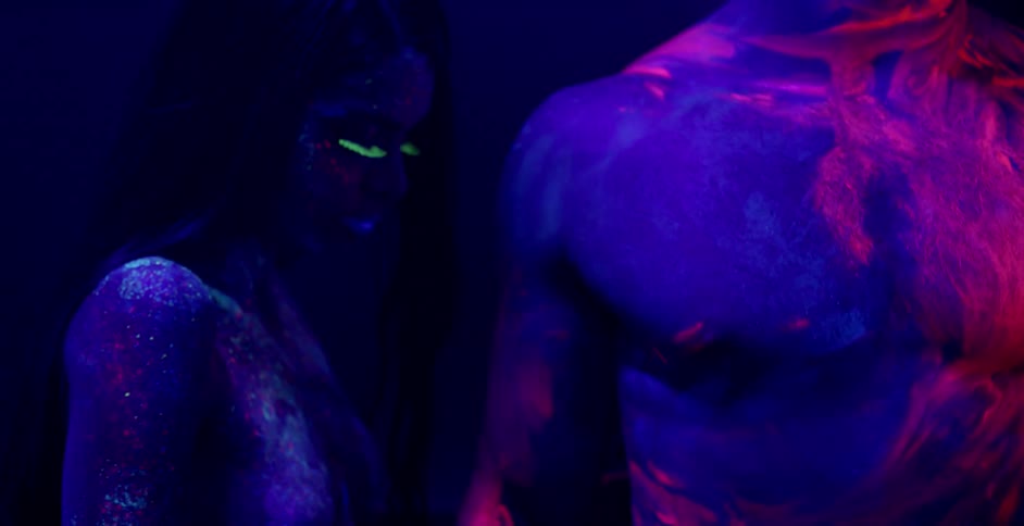 A man and woman rub glowing body paint on each other