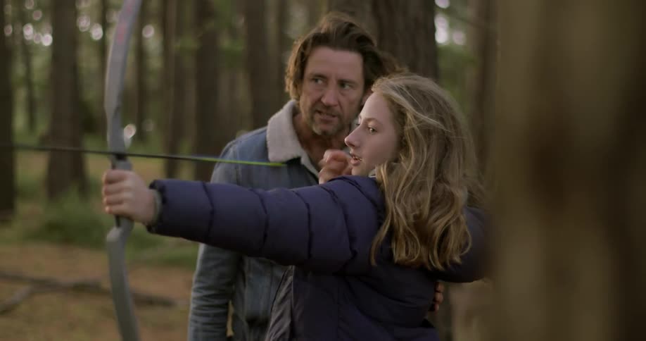 A man is teaching a young girl how to shoot a bow and arrow