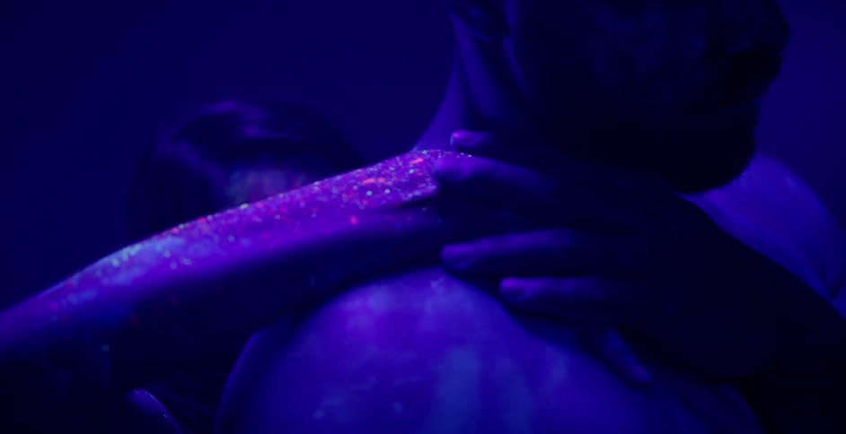 Woman covered in glowing paint touches a man