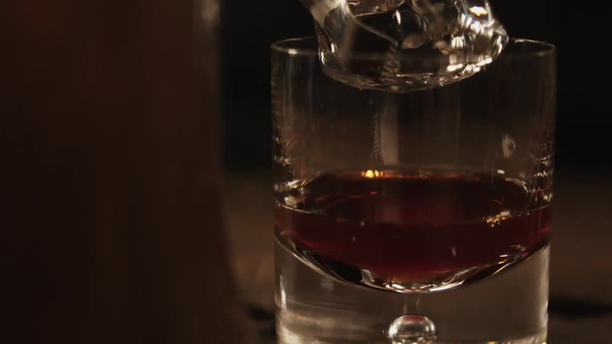 An ice cube is being added to a whiskey drink
