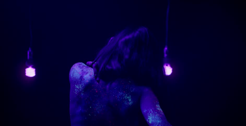 A woman in body paint dances by hanging black lights